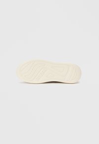 Krémová podešev tenisky s texturovanými drážkami a brandingem. Vyznačuje se hladkým povrchem a zaobleným designem špičky pro pohodlí.