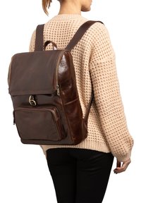 Zaino in pelle marrone con scomparto principale con zip, tasca frontale e spallacci regolabili. Caratterizzato da una texture liscia e da accessori metallici lucidi.