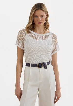 White textured knit top with short sleeves, featuring a geometrical pattern. Paired with high-waisted, cream-colored trousers and a braided navy belt.