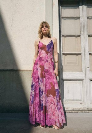 Robe longue à fleurs dans des tons de rose et de violet, avec des bretelles spaghetti et un design fluide. Le matériau semble léger et transparent.