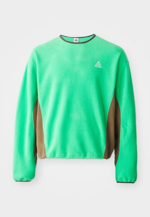 Zaļš flīsa krekls ar brūniem sānu paneļiem, garām piedurknēm un apaļu kakla izgriezumu ar nelielu logo uz krūtīm.