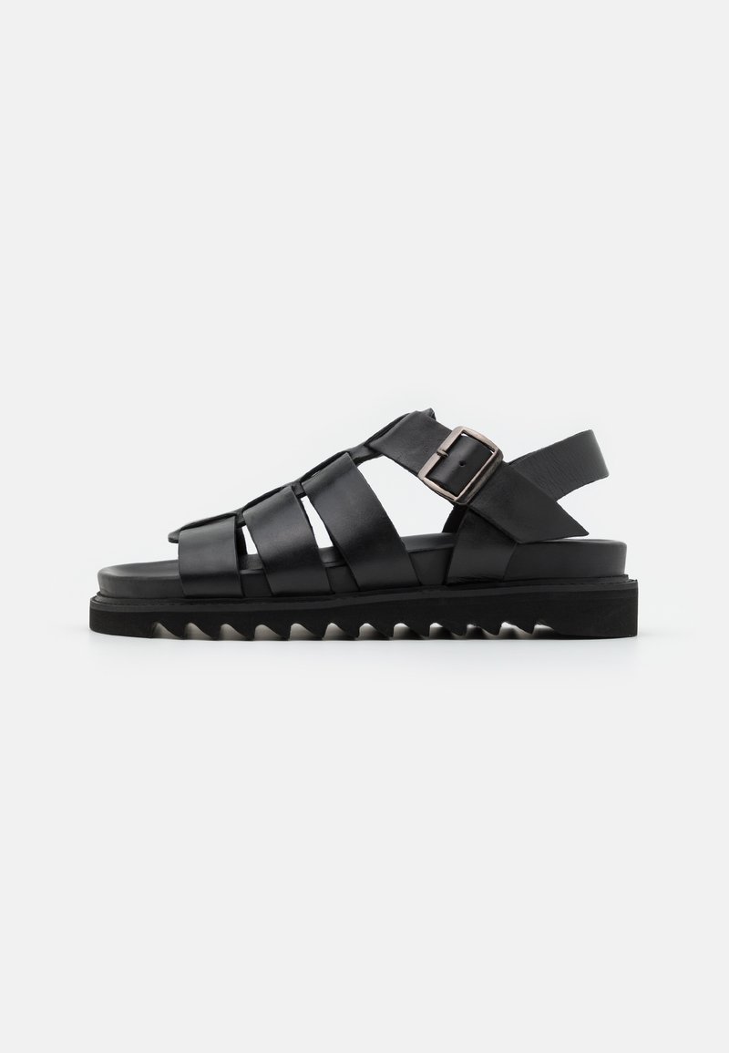 Zwarte leren sandalen met een strappy ontwerp, een verstelbare gesp en een geribbelde zool voor grip. Voorzien van een platte voetbed en een open achterkant.