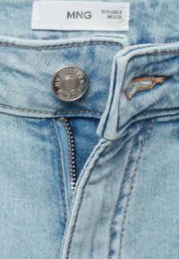 Svetlomodré džíny z denimu s kovovým gombíkom s gravírovanou značkou, zapínaním na zips a kontrastným šitím pozdĺž okrajov.