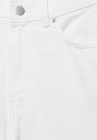 Detail bielych rifľov z denimu zobrazujúci kovový gombík, nit, slučku na opasok a detail šitia vrecka.