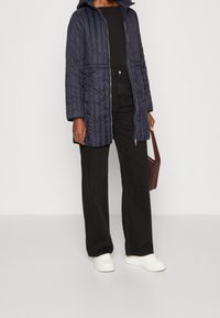 Abrigo de plumas acolchado azul marino con capucha, cierre frontal, bolsillos laterales y un diseño texturizado; combinado con pantalones negros y zapatillas blancas.