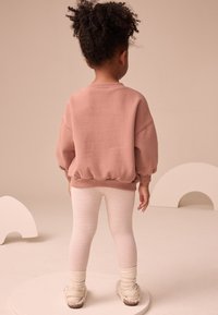 Prašná ružová mikina voľného strihu s rebrovanými manžetami, doplnená svetlými pruhovanými legínami. Mäkké, textúrované materiály, útulný dizajn.