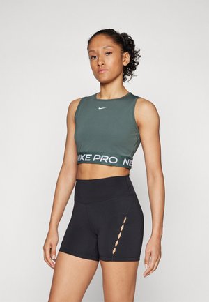 Grønn Nike croppet topp med hvit logo og svart Nike Pro midjebånd, kombinert med høytwastet svarte shorts med utskjæringsdetaljer.