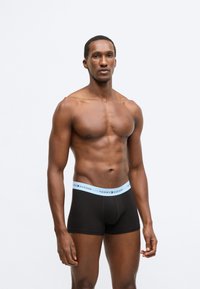 Mustad bokserid helesinise elastse vöökohaga, millel on "TOMMY HILFIGER" logo. Sile tekstuur ja kehale istuv disain.