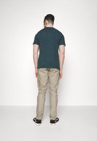 Mørkegrøn kortærmet T-shirt, beige bukser og sorte sneakers. Simpelt design med en afslappet pasform uden synlige mønstre eller accenter.