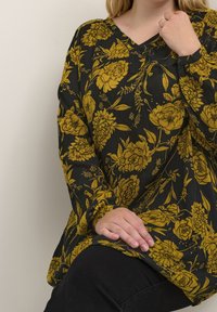 Zwarte bloemen tuniek met geel bloemenpatroon, V-hals ontwerp en lange mouwen, gemaakt van textuurstof, gecombineerd met zwarte broek.