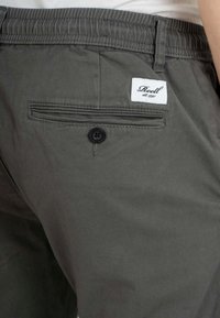 Pantalones cortos de color gris oscuro, fabricados en un tejido ligero, con una cintura elástica, un bolsillo trasero con botón y una etiqueta blanca cosida.