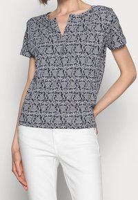 Blusa de manga corta con fondo azul marino y patrón de paisley blanco, presenta un escote en V y una tela suave y ligera.
