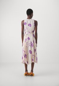 Abito midi a stampa floreale in crema con fiori viola, design senza maniche, vita cinchata e silhouette fluida. Scarpe con tacco arancioni con dettagli in pelliccia.