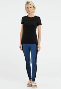 Čierny krátky rukáv športový top v kombinácii s legínami s modro-čiernymi panelmi; hladká látka, priliehavý strih a ploché švy pre pohodlie.