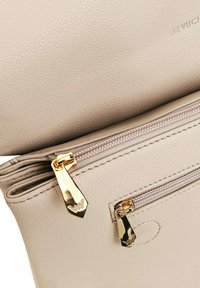 Beige texturovaná kožená kabelka s pozlacenými zipy a kovovými prvky, s jedním hlavním prostorem a menší vnější kapsou na zip.