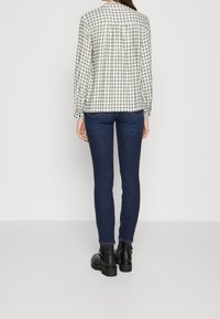 Chemise à carreaux blancs et noirs à manches longues, cintrée aux poignets, accompagnée d'un jean ajusté bleu foncé et de bottines noires.