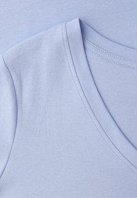 Lyseblåt bomuldstof, der viser et close-up af en V-hals krave og skuldersøm med synlige sting.