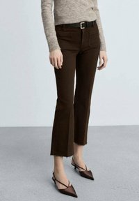 Brune klokkejeans med flosset bund, forlommer og et sort bælte med en guldspænde. Båret med spidse brune hæle.