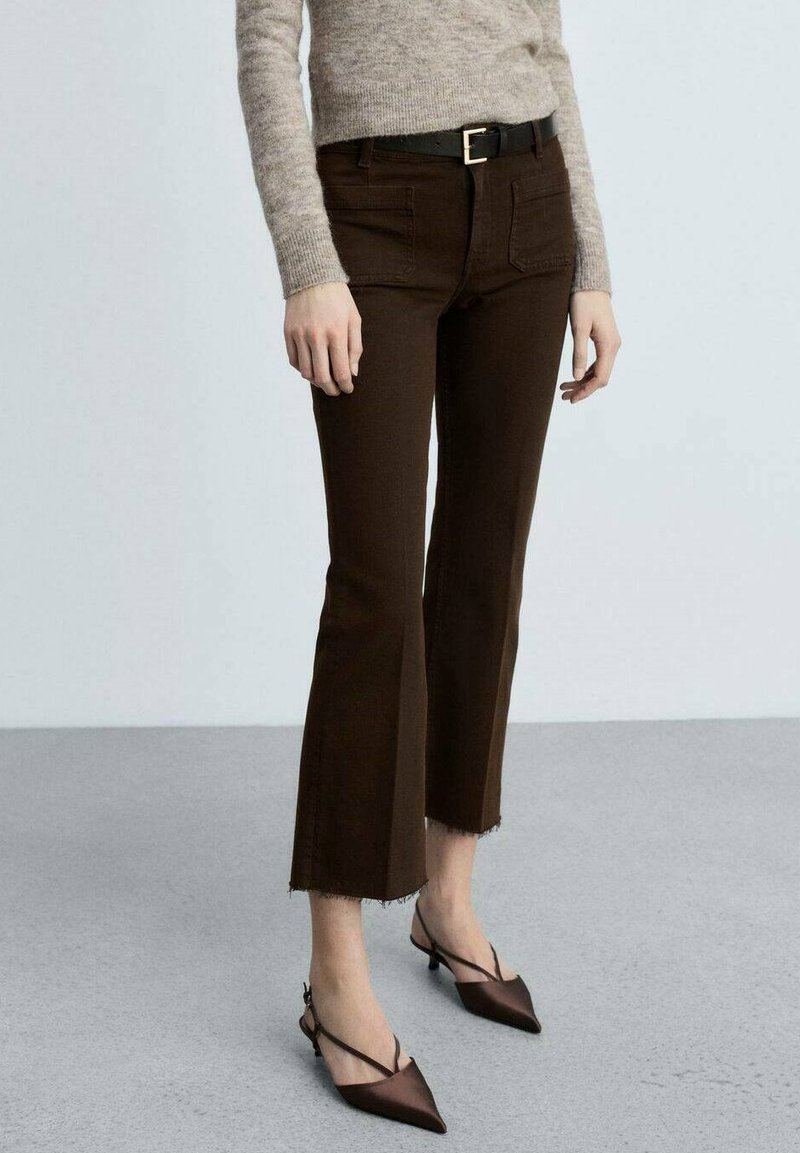 Brune klokkejeans med flosset bund, forlommer og et sort bælte med en guldspænde. Båret med spidse brune hæle.