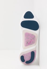 Semelle de chaussure Nike blanche avec des accents bleus et roses. Présente un motif de traction texturé et un amorti à air visible à travers une découpe transparente.