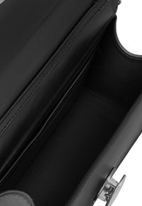 Wnętrze czarnej skórzanej torebki o gładkiej teksturze, z centralną komorą i srebrnym okuciem do zamykania.