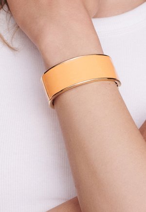 Wide orange bangle bracelet with a smooth finish, metallic gold accents, and a flat, rectangular shape on a wrist.