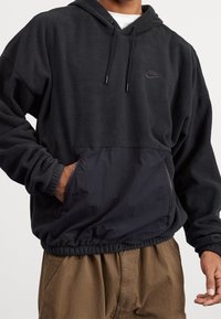 Svart fleece hoodie med känguruficka, elastiska ärmar och nederkant. Har en kontrasterande nylonpanel nedtill och en subtil logotyp.