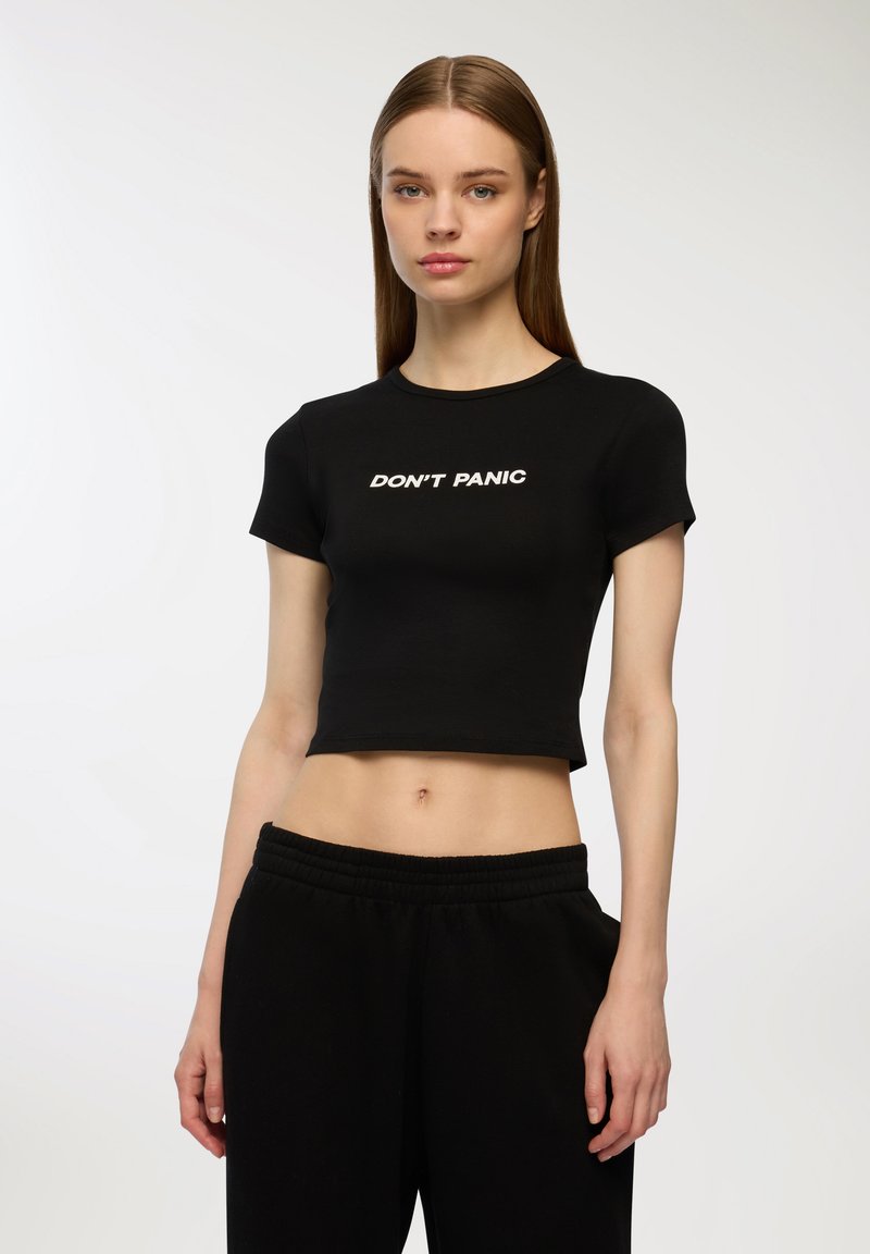 T-shirt nero cropped in cotone, con maniche corte e scritta bianca "NON ENTRARE IN PANICO" sul davanti, abbinata a pantaloni neri con vita elastica.