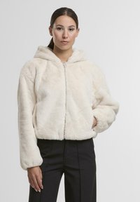 Faux-Fur-Jacke mit Kapuze in Off-White, mit einem Frontreißverschluss, langen Ärmeln und einem samtigen Material. Kombiniert mit schwarzen, figurbetonten Hosen.