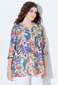 Tunic floreale con scollatura a V e maniche a tre quarti. Realizzata in tessuto leggero con fiori e foglie vivaci nei colori verde, arancione e blu.