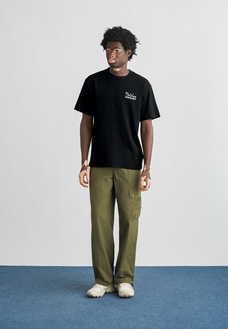 Black cotton t-shirt with "Dickies" logo, paired with loose olive green cargo pants featuring side pockets and a textured finish. Beige sneakers.