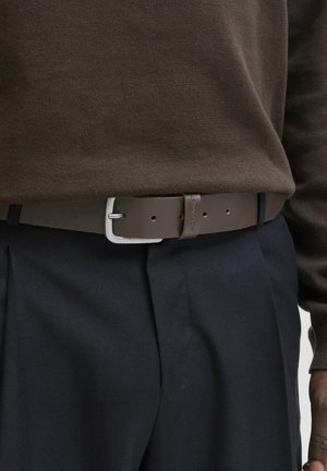 Brown leather belt with a silver-colored buckle and a textured finish, worn over navy trousers and a dark brown sweater.