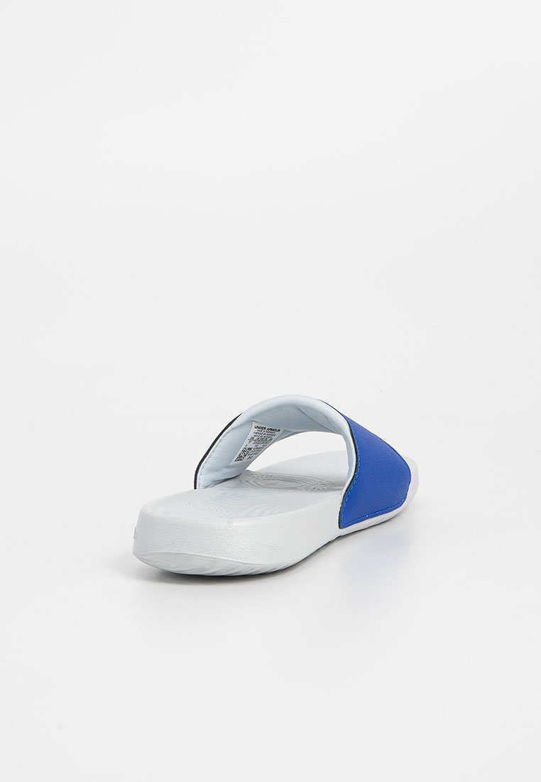 Sandalia blanca con una tira ancha azul y una plantilla texturizada, vista desde atrás sobre un fondo blanco.