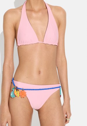 Kobieta ubrana w jasnoróżowy bikini typu halter z niebieskim paskiem z koralików z kolorowymi zawieszkami w kształcie owoców i kwiatów wokół bioder.
