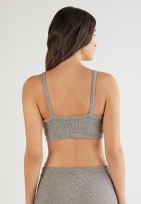 Bralette tricoté gris avec une texture côtelée, des bretelles fines et un design sans coutures, présentant une couleur unie sans motifs ni accents supplémentaires.