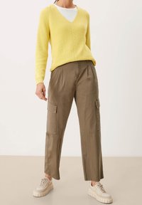 Gelber Strickpullover mit V-Ausschnitt und strukturiertem Stickmuster, kombiniert mit khakifarbenen Cargo-Hosen mit seitlichen Taschen und einer lockeren Passform.