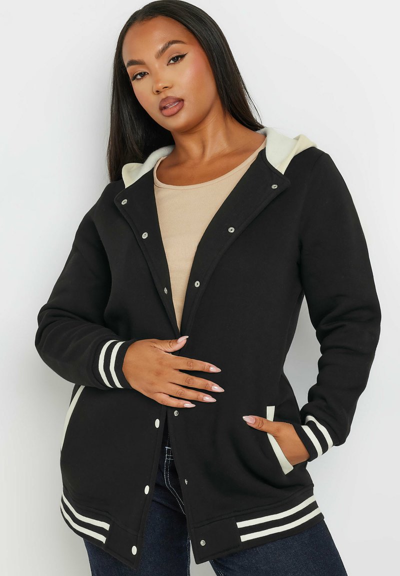 Schwarze Kapuzenjacke mit gestreiften weißen Akzenten, Druckknöpfen und seitlichen Taschen. Weicher Stoff mit glatter Textur.