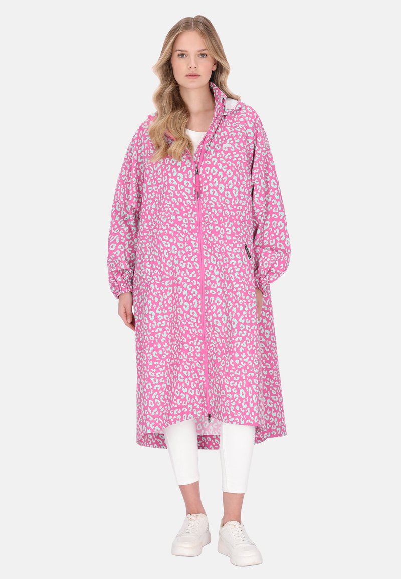 Dlouhý kabát s růžovým leopardím vzorem, zapínáním na zip, měkkou texturou a elastickými manžetami, nošený přes bílé tričko a bílé legíny.
