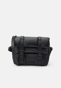 Borsa a tracolla in pelle nera con due cinturini con fibbia sul davanti e logo "Dr. Martens" in rilievo sulla pattina frontale.