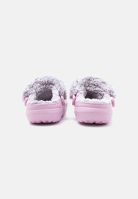 Un paio di zoccoli rosa senza lacci con una morbida fodera bianca, visti da dietro su uno sfondo bianco.