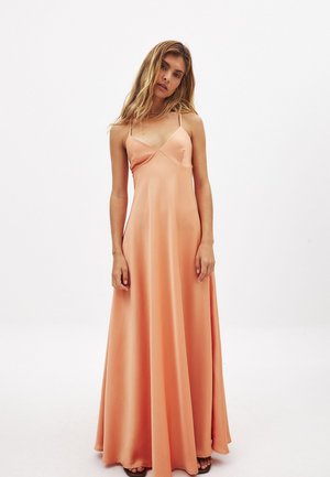 Dlhé, bezrukávové šaty z jemnej broskyňovej látky. Majú výstrih do V, nastaviteľné tenké ramienka a voľný strih. Hladká textúra.