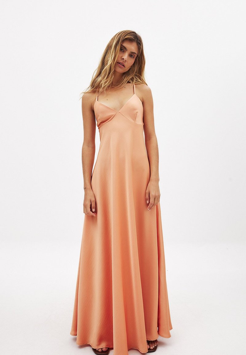 Pitkä, hihaton mekko pehmeästä persikkakankaasta. Ominaisuuksiin kuuluvat V-pääntie, säädettävät ohutolkaimet ja virtaava siluetti. Sujuva tekstuuri.