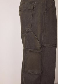 Dunkelgraue Cargo-Hosen aus strukturiertem Stoff, mit mehreren Taschen und einem einzigartigen Nahtdesign entlang der Seite.