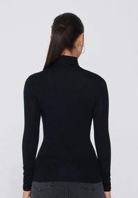 Haut à manches longues noir avec un col montant, fabriqué en tissu lisse et extensible. Présente une coupe ajustée et un design minimaliste.