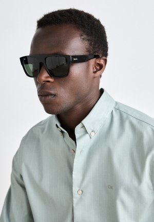 Zwarte Ray-Ban zonnebril met grijze lenzen, gedragen met een lichtgroen gestreept overhemd met knopen en een CK-logo op de borst.