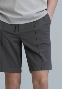 Shorts gris en tissu léger, dotés d'une taille à cordon de serrage, de poches latérales et de coutures verticales pour un look ajusté.
