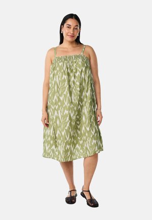 Vestido verde con estampado, con tirantes finos ajustables, cuerpo rizado y un diseño suelto y fluido que llega hasta la mitad de la pantorrilla. Se lleva con sandalias negras.