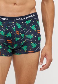 Tengerészkék boxer alsó ünnepi karácsonyfás mintával, zöld fák és narancssárga "HOLLY JOLLY" felirattal. Rugalmas derékpánt logóval.