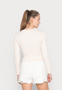 Top de manga longa de cor rosa claro, feito de tecido canelado, design ajustado, vista traseira. Combinado com calções brancos rasgado, destacando detalhes de bainha crua.