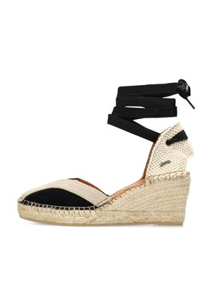 Espadrille wedge sandal features a woven jute sole, black fabric accents, beige canvas upper, and crisscross black ankle ties.